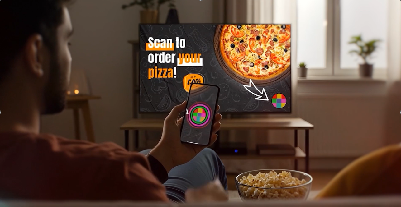 Viewer scans an interactive Qapture marker on a TV pizza ad with a smartphone, enabling real-time audience engagement and ordering directly from the broadcast screen.